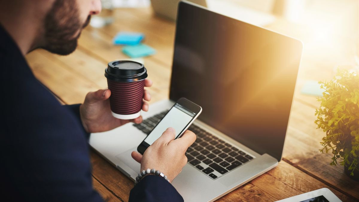 Mesa de trabalho com celular aberto em rede social ao lado de um notebook