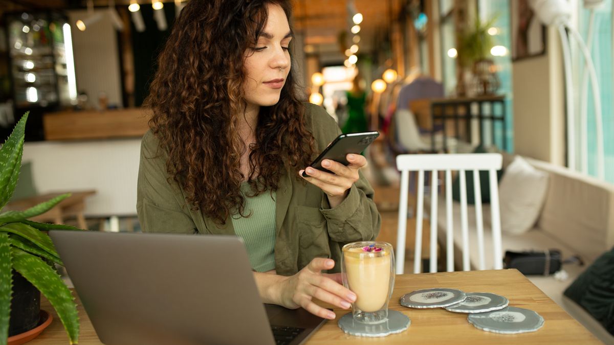 Pessoa em um café usando notebook e segurando o celular ao mesmo tempo